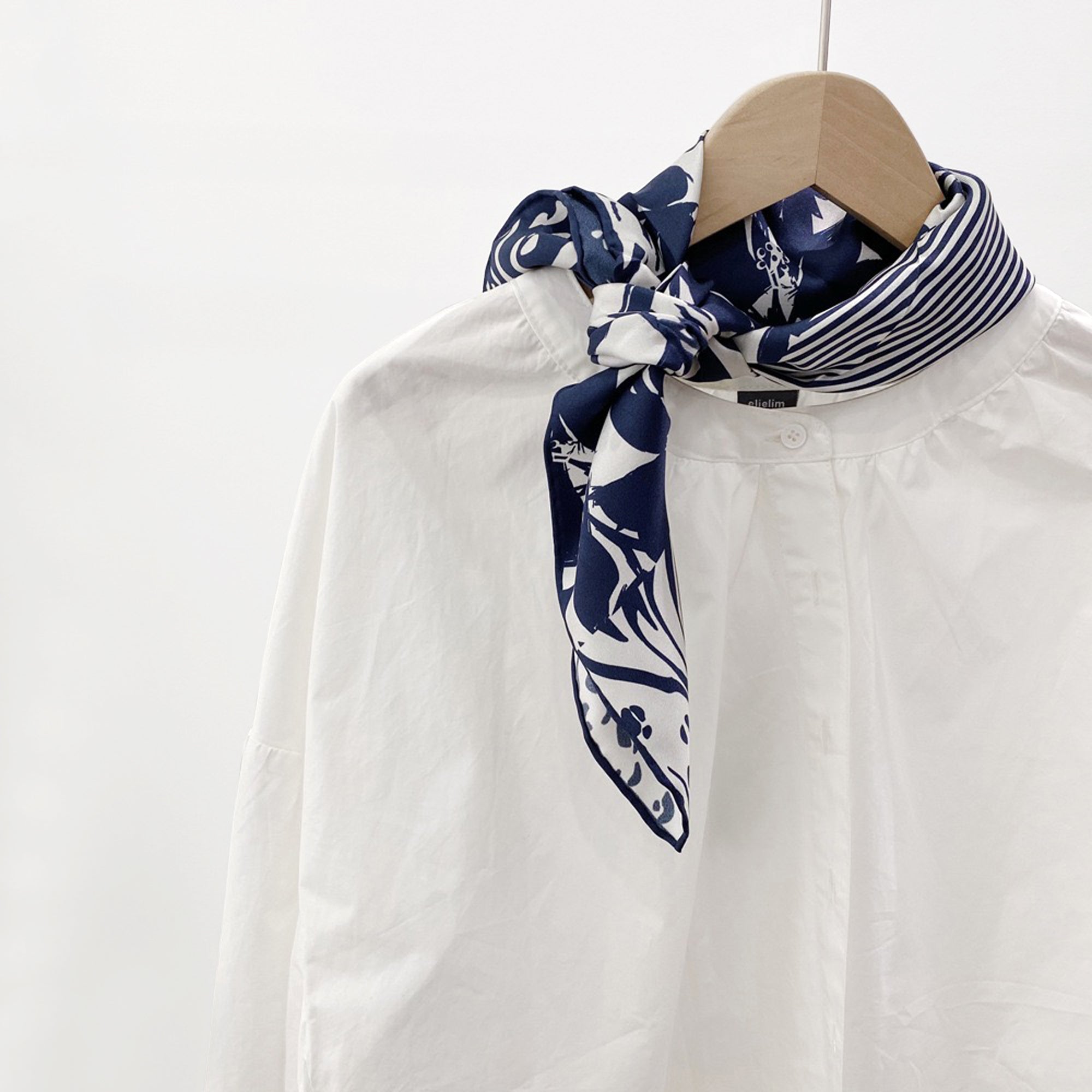 a blue and white printed silk scarf with hand-rolled edges, knotted around the neck as a neck scarf, paired with a women's white blouse