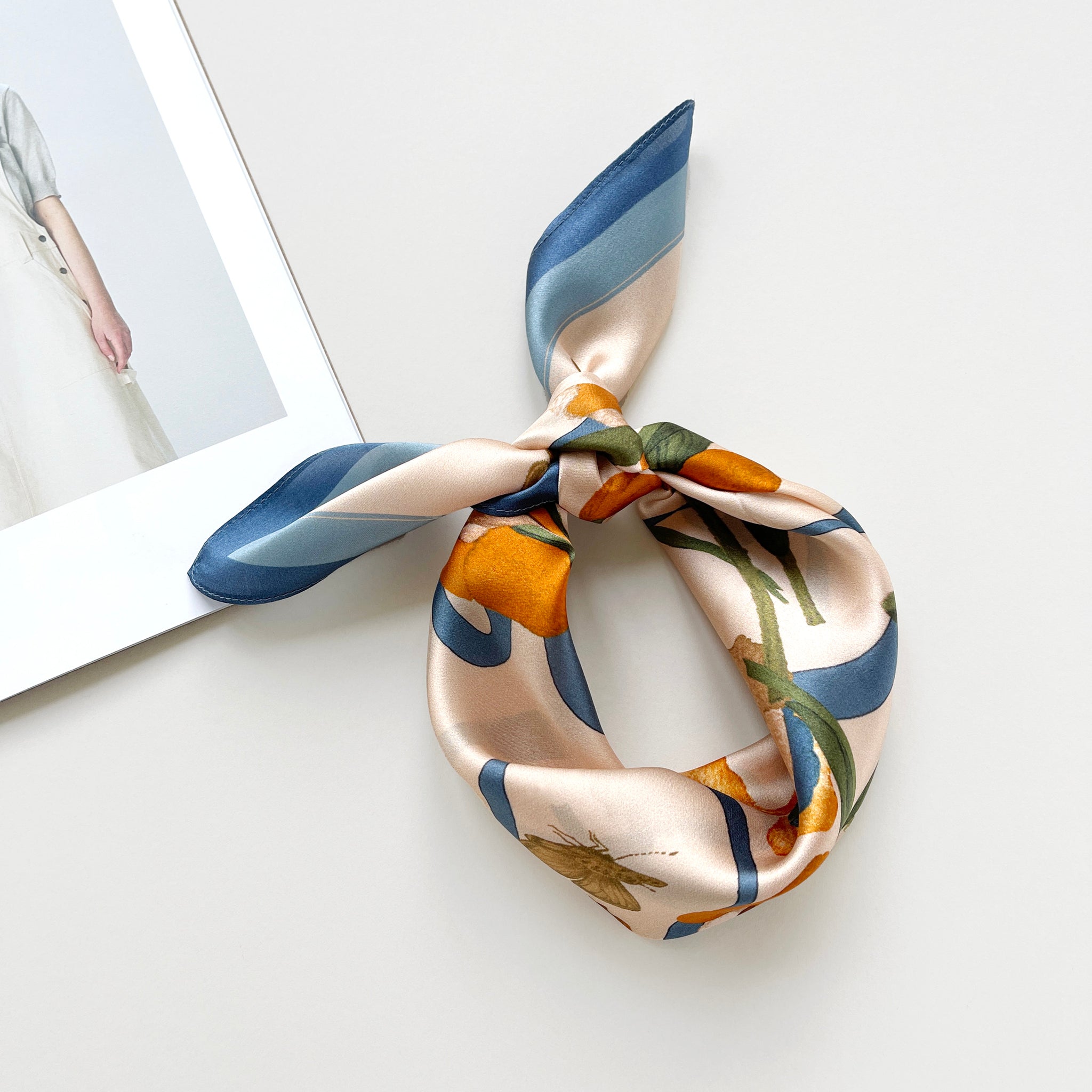 a silk bandana scarf featuring lily and butterfly print, knotted as a head scarf