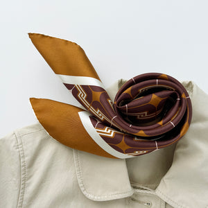 a luxury silk scarf featuring 70s style patten in burgundy, tan and beige palette with hand-rolled hems, paired with a beige coat