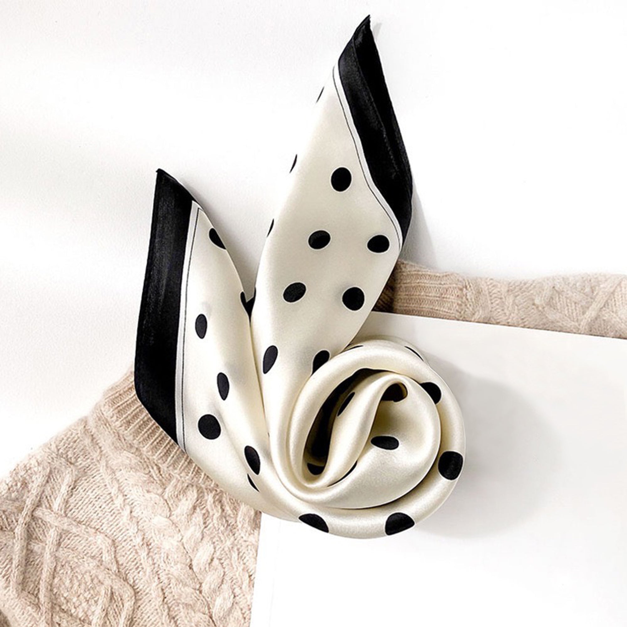 a classic black and white polka dot silk bandana scarf paired with a beige sweater 