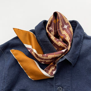 65x65cm brown silk scarf with a geometric pattern and hand-rolled edges, featuring a contrasting border. Retro-inspired unisex accessory, perfect for versatile styling around the neck, hair, or as an accent piece.