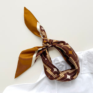 a luxury silk scarf featuring 70s style patten in burgundy, tan and beige palette with hand-rolled hems, knotted as a headband