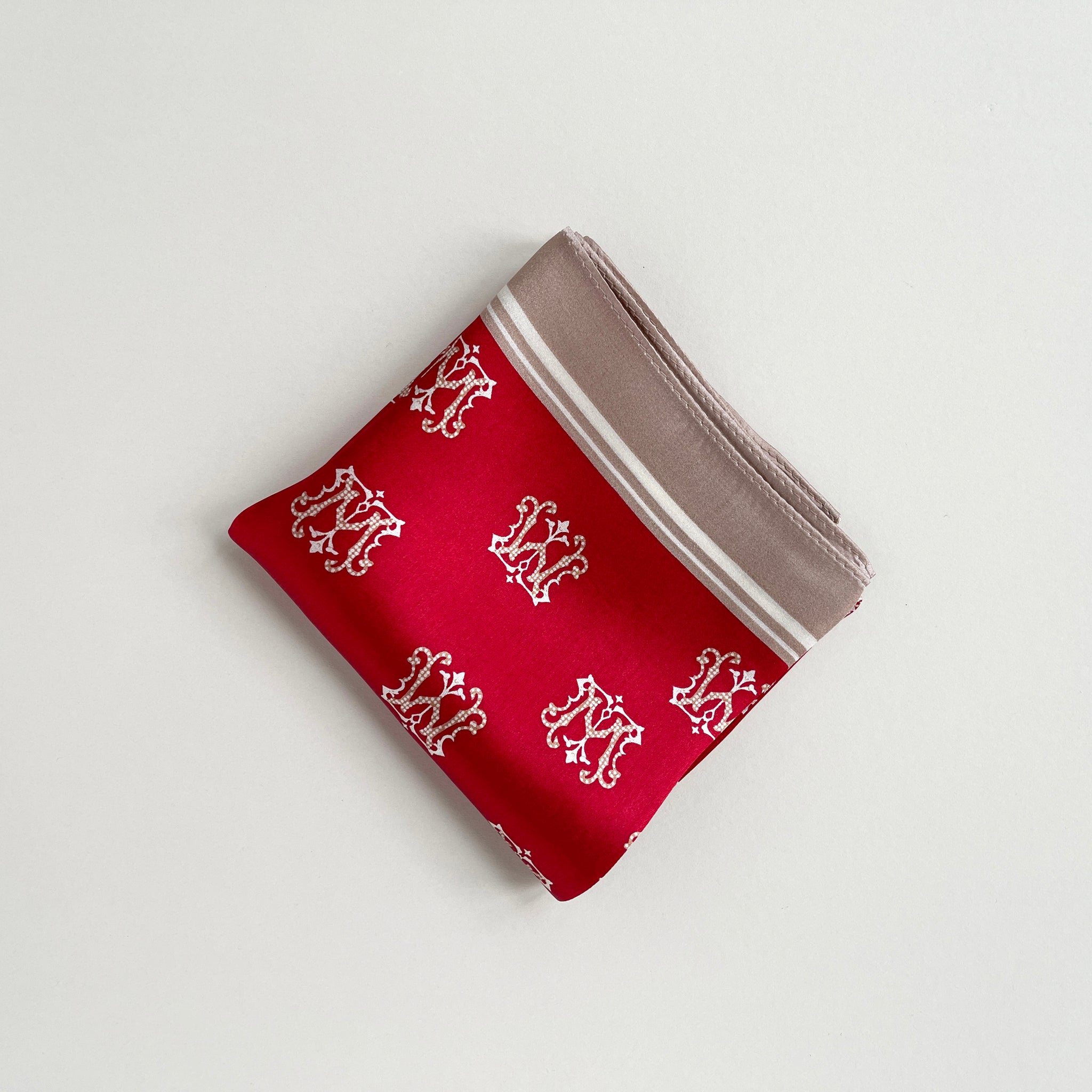 a red small silk scarf with beige edge featuring crown print folded in a square shape
