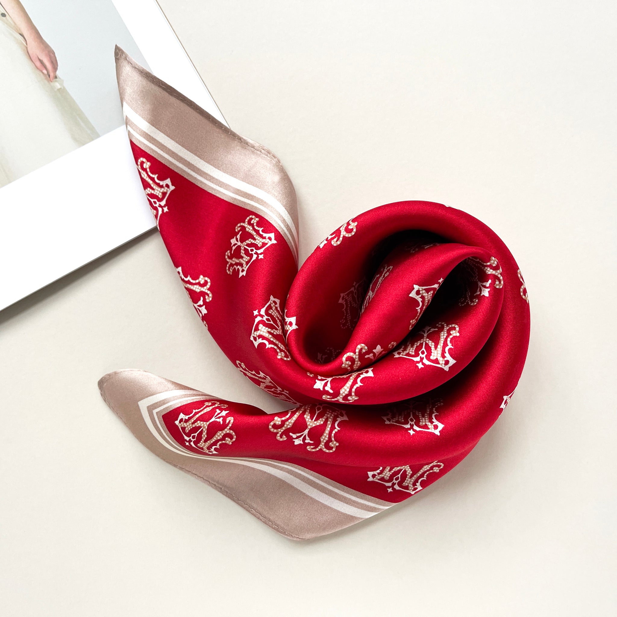 a red small silk scarf with beige edge featuring crown print