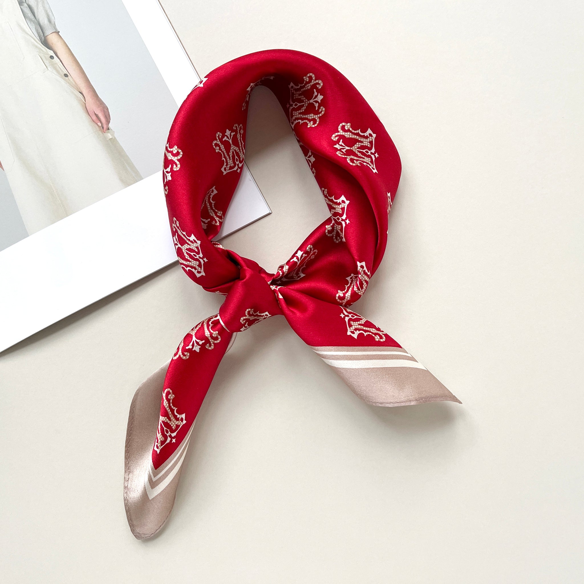 a red small silk scarf with beige edge featuring crown print, knotted as neckerchief 