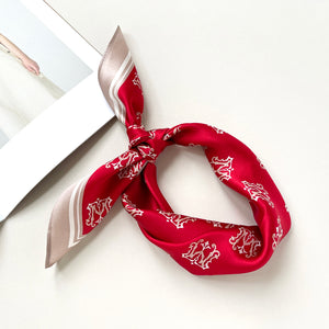 a red small silk scarf with beige edge featuring crown print, knotted as neckerchief or headband