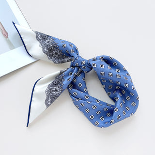 a cerulean blue square silk scarf with white base and navy blue hand-rolled hems, featuring boho style print, knotted as a neckerchief or headband