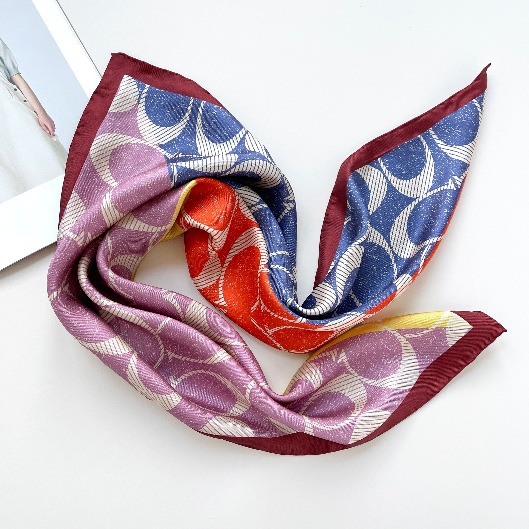 a luxury square silk scarf in lilac oink, blue, orange and yellow featuring burgundy hand-rolled edges and classic print