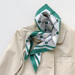 a turquoise square silk scarf with light grey base, featuring simplified floral print, paired with a beige coat