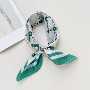 a turquoise square silk scarf with light grey base, featuring simplified floral print, knotted as a neckerchief 