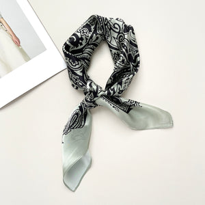 a pale pea green silk scarf with black boho style print, knotted as a classic neckerchief