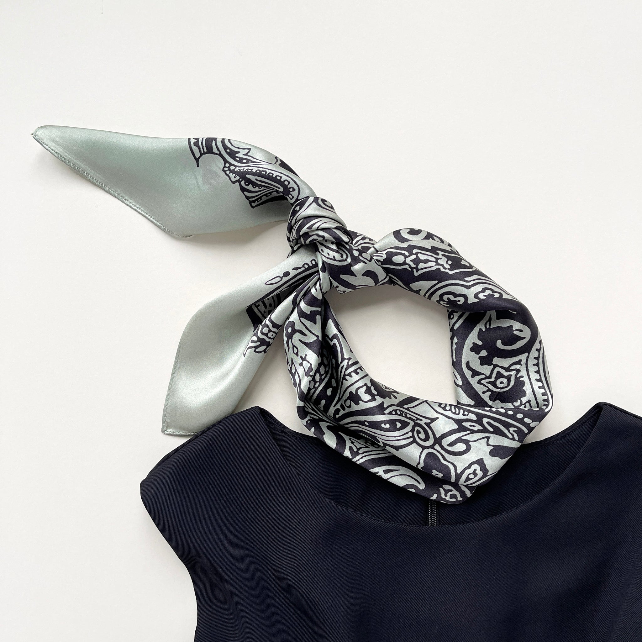 a pale pea green silk scarf with black boho style print, knotted as a neckerchief or headband, paired with a black sleeveless dress