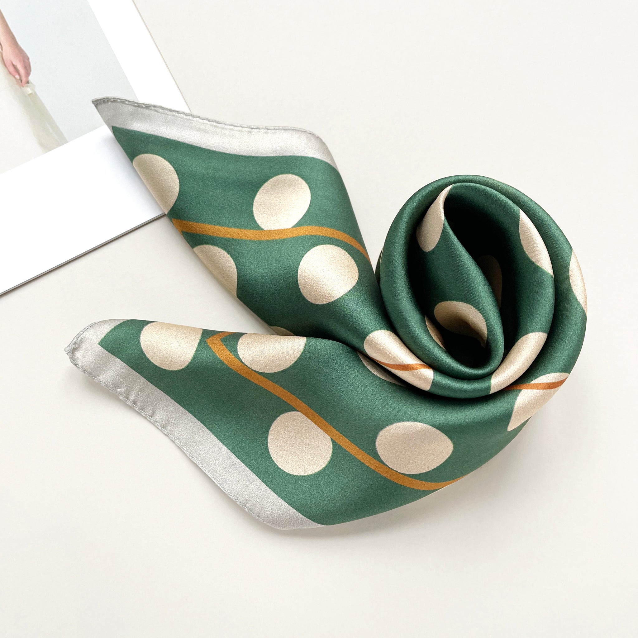 a jade green silk scarf bandana featuring light beige polka dot print and mustard yellow line near the edge