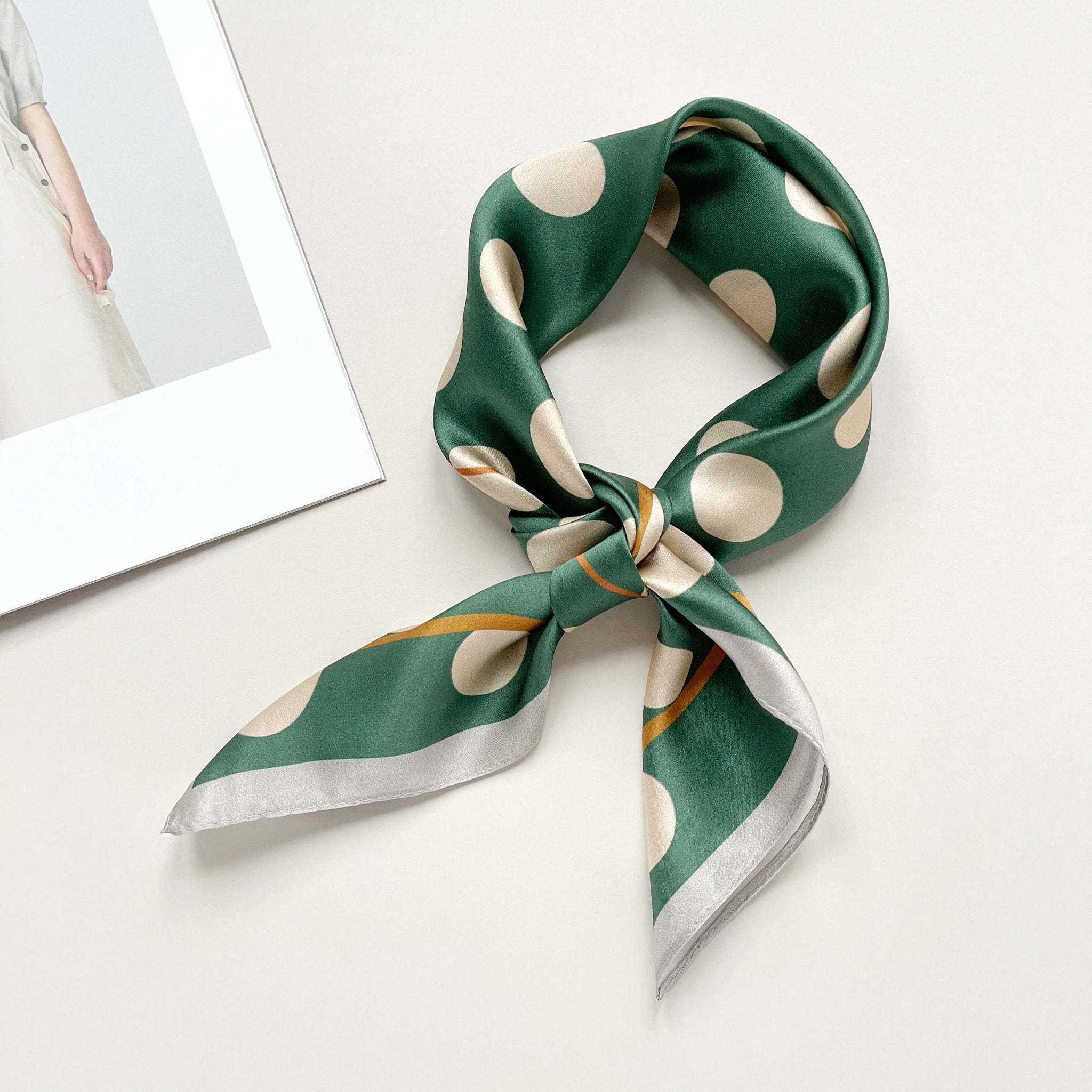 a jade green silk scarf bandana featuring light beige polka dot print, knotted as a neckerchief 