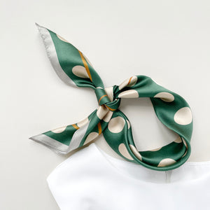 a jade green silk scarf bandana featuring light beige polka dot print and mustard yellow line near the edge, knotted as neckerchief or headband, paired with a white sleeveless dress
