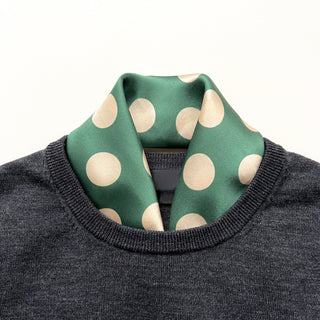 a jade green silk scarf bandana featuring light beige polka dot print and mustard yellow line near the edge, tucked in a dark grey men's sweater