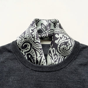 a pale pea green silk scarf with black boho style print tucked in a dark grey men's sweater 