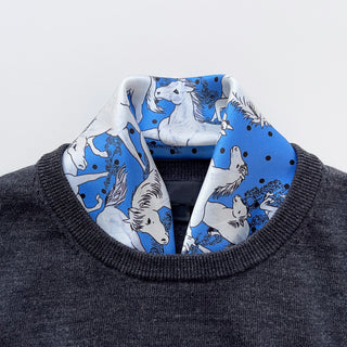 a bright blue men's silk scarf featuring classic horse riding and paisley prints with navy blue edge, tucked in a dark grey men's sweater 