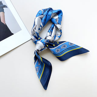 a bright blue men's silk scarf featuring classic horse riding and paisley prints with navy blue edge, knotted as a neckerchief 