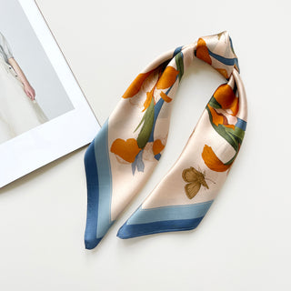 a small silk scarf in sky blue and orange featuring lily and butterfly prints knotted as a ponytail 