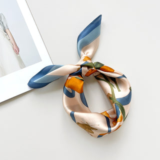 53x53 bandana silk scarf in sky blue and orange featuring lily and butterfly prints knotted as a headband.