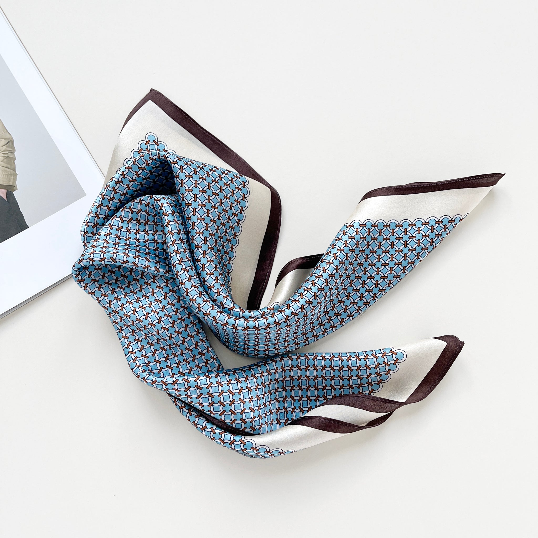 a small square silk scarf with brown edge featuring sky blue circle print