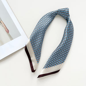 a small square silk scarf with brown edge featuring sky blue circle print, knotted as a poneytail