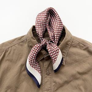 a silk scarf with navy blue edge featuring red circle print, knotted as a mens neckerchief, paired with a men's khaki shirt