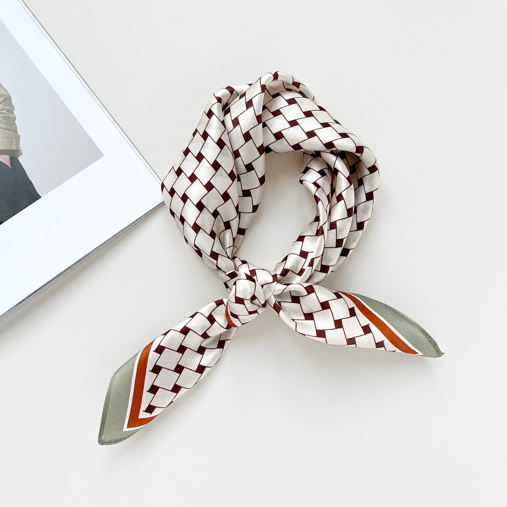 a white base pinted silk bandana scarf with pea green and orange edge, featuring burgundy geometric block print, knotted as a classic neckerchief