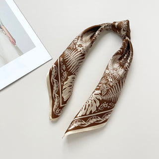 a bronze silk bandana scarf featuring beige botanic leaf print, knotted as a ponytail 