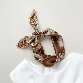 a bronze silk bandana scarf featuring beige botanic leaf print, knotted as a headband