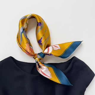 vintage vibe silk bandana scarf in vibrant mustard yellow featuring flowers and butterflies print with dark blue edge, knotted as a neck scarf, paired with a black dress