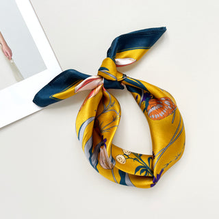 vintage vibe silk bandana scarf in vibrant mustard yellow featuring flowers and butterflies print with dark blue edge, knotted as a headband