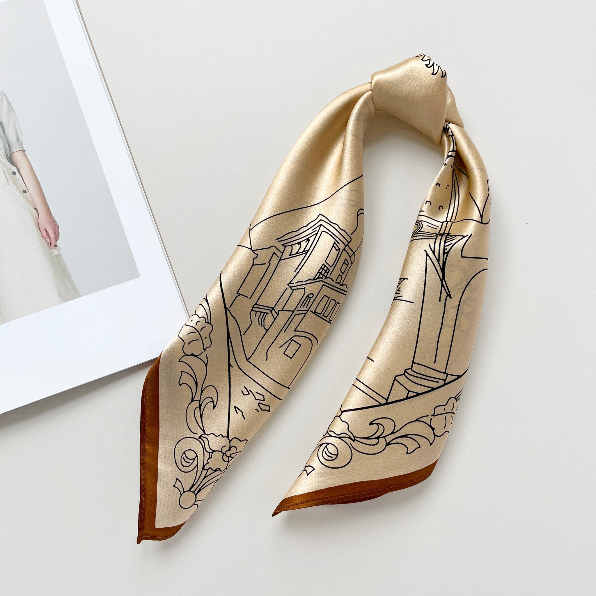a timeless pale apricot silk bandana scarf featuring black print with brown edge tied as a ponytail