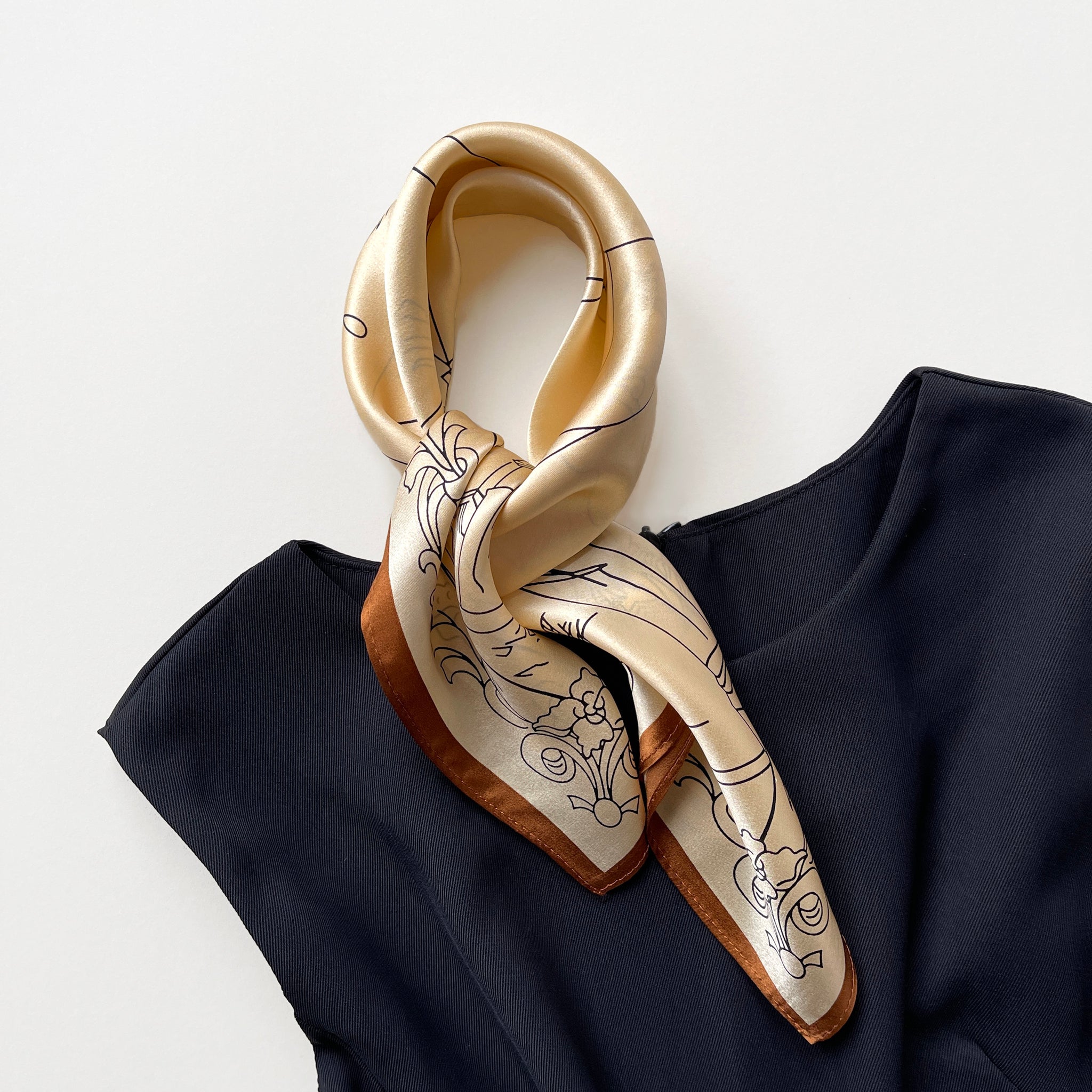 a timeless pale apricot silk bandana scarf featuring black print with brown edge tied as a neck scarf, paired with a black sleeveless dress