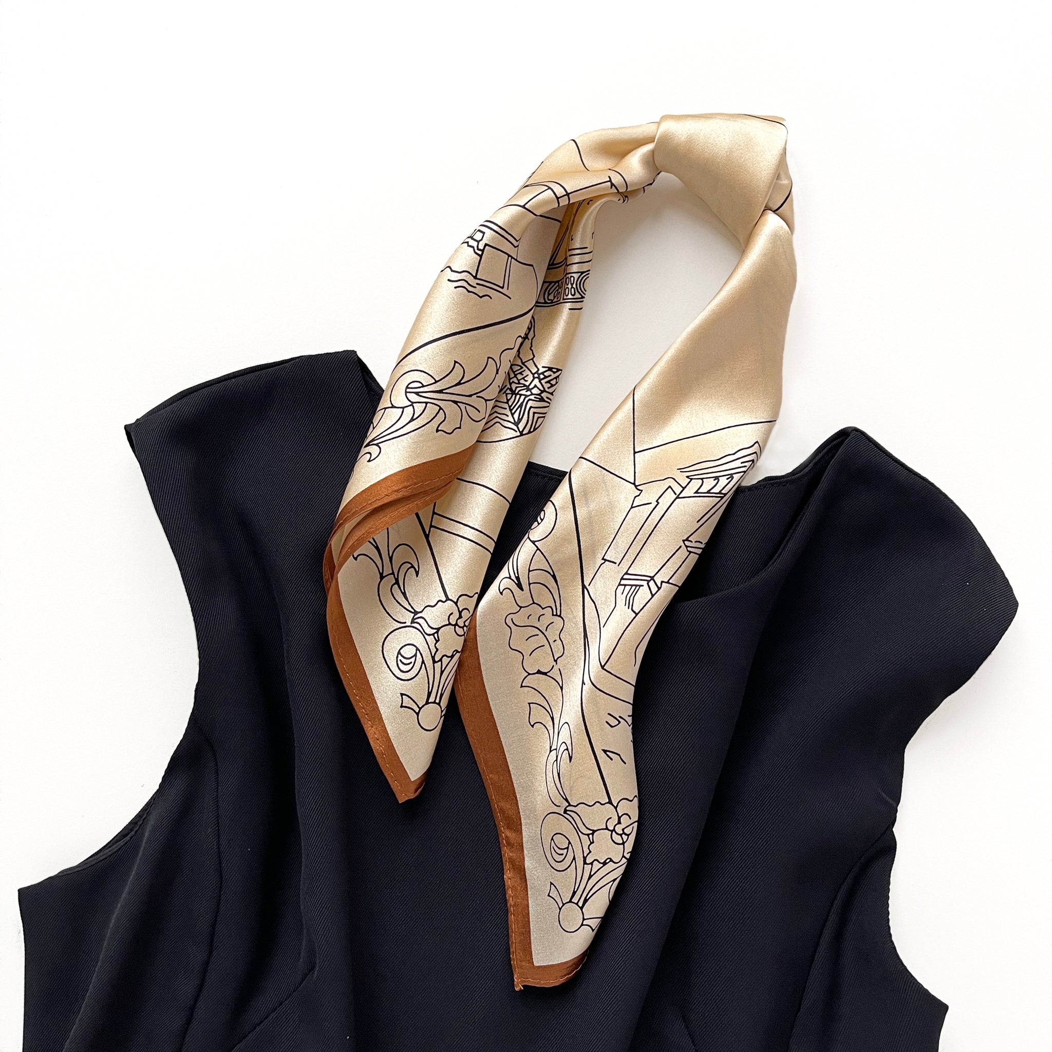 a timeless pale apricot silk bandana scarf featuring black print with brown edge tied as a ponytail, paired with a black sleeveless dress