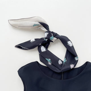 a luxury floral rose black silk scarf with beige edge, featuring hand-rolled hems, tied as a neck scarf, paired with a sleeveless black dress