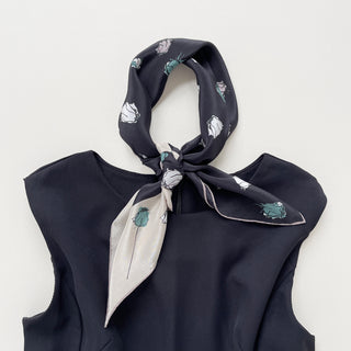 a luxury floral rose black silk scarf with beige edge, featuring hand-rolled hems, tied as a classic neckerchief, paired with a sleeveless black dress