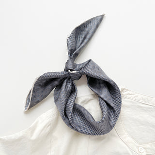 a classic silk scarf neckerchief featuring black and white checks and navy blue polka dots with white hand-rolled hems, knotted as a headband, paired with a light beige shirt