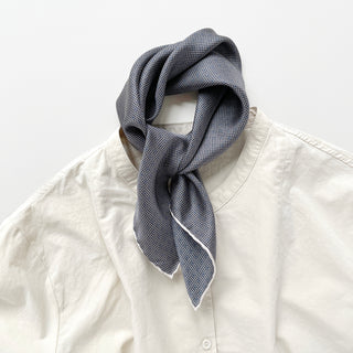 a classic silk scarf neckerchief featuring black and white checks and navy blue polka dots with white hand-rolled hems, knotted as a neck scarf, paired with a light beige shirt