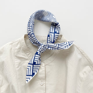 Unisex silk bandana with a white base and blue geometric pattern, featuring hand-rolled hems for an elegant finish. Versatile accessory for men and women, perfect for wearing around the neck or in the hair.