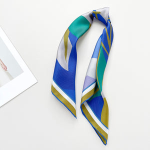 an abstract lotus print square silk scarf in blue, green, lilac and mustard yellow palette with hand-rolled hems knotted as a ponytail 
