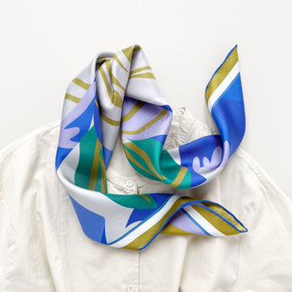 an abstract lotus print square silk scarf in blue, green, lilac and mustard yellow palette with hand-rolled hems paired with a light beige women's turtle neck shirt