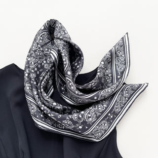 65cm square silk scarf with a black and white paisley print and hand-rolled edges, designed for men and women. Luxurious, soft silk accessory, versatile for wearing around the neck, as a headscarf, or styled on a handbag.