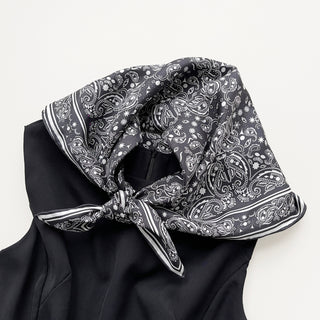 a black and white silk scarf neckerchief featuring bohemian paisley print with hand-rolled edges, tied around the shoulder, paired with a black dress