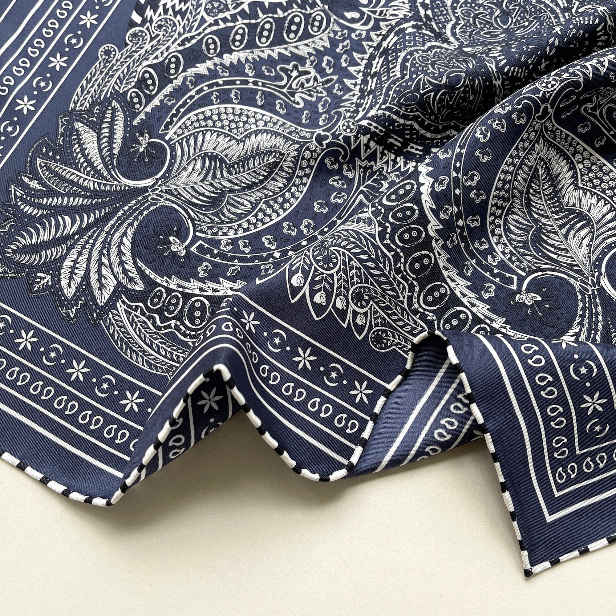 a navy blue bandana silk scarf featuring white and black symmetric pattern with striped hand-rolled edges