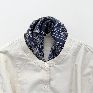a navy blue bandana silk scarf featuring white and black symmetric pattern with striped hand-rolled edges, tucked in a light beige turtle neck shirt