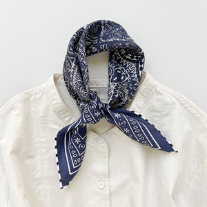 a navy blue silk bandana scarf featuring white and black symmetric pattern with striped hand-rolled edges, tied as a neckerchief, paired with a light beige turtle neck shirt