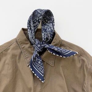 a navy blue mens neckerchief silk scarf featuring white and black symmetric pattern with striped hand-rolled edges, knotted as a neckerchief, paired with a khaki men's shirt