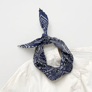 a navy blue silk bandana scarf featuring white and black symmetric pattern with striped hand-rolled edges, tied as a headband or neck scarf, paired with a light beige turtle neck shirt